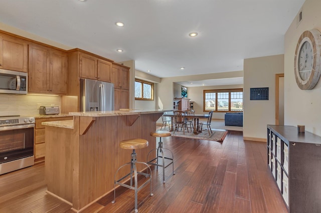 kitchen featuring a wealth of natural light, appliances with stainless steel finishes, dark wood-type flooring, and a kitchen breakfast bar