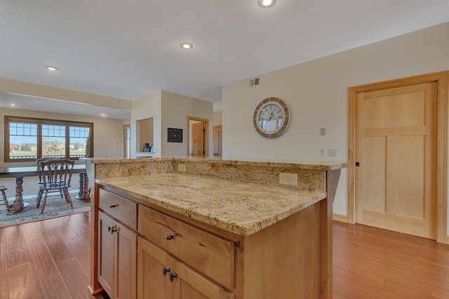 kitchen with light stone counters, visible vents, a center island, and light wood finished floors