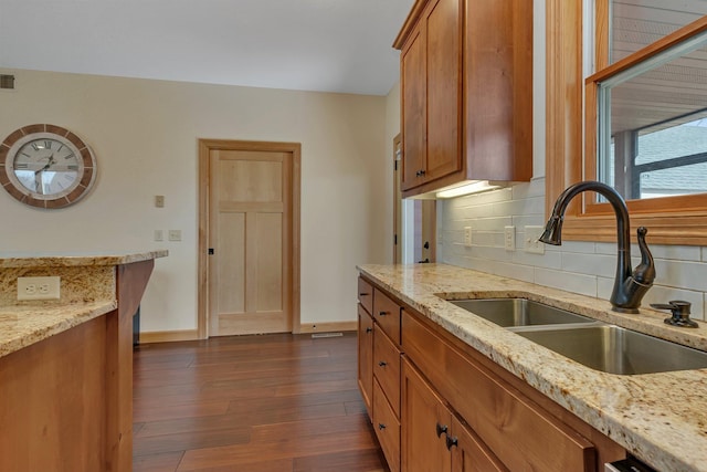 kitchen with brown cabinetry, dark wood-style flooring, decorative backsplash, and a sink