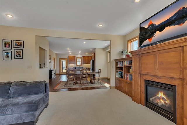 living room featuring a glass covered fireplace, wood finished floors, recessed lighting, and baseboards