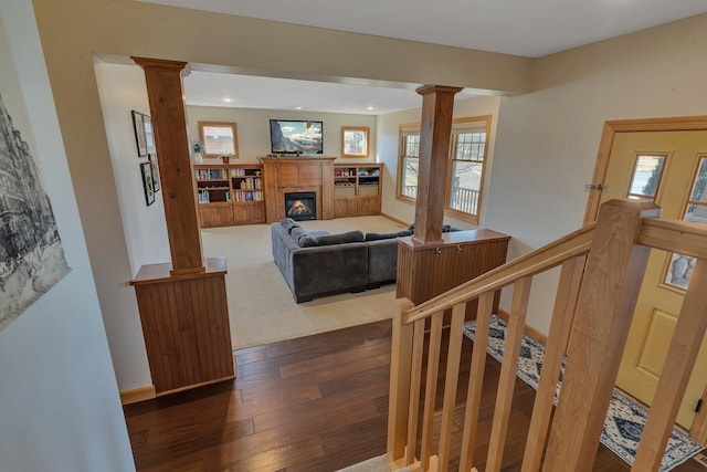 living room featuring hardwood / wood-style floors, a glass covered fireplace, recessed lighting, decorative columns, and baseboards