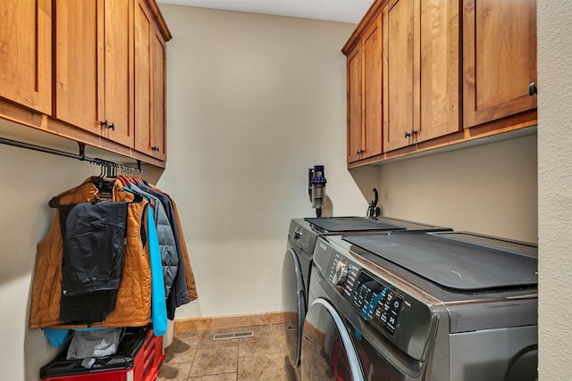 laundry area featuring washing machine and clothes dryer, visible vents, stone finish flooring, baseboards, and cabinet space