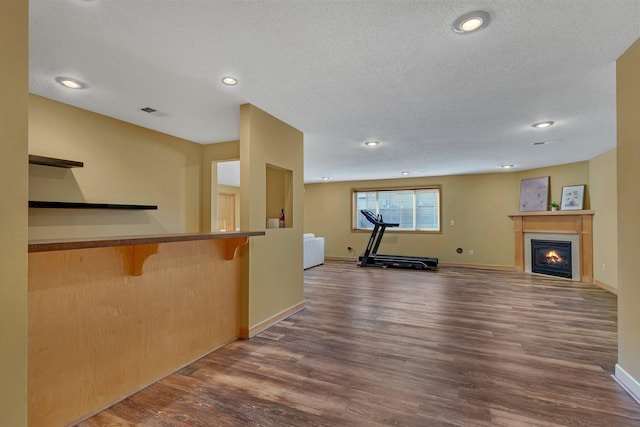 exercise area with a glass covered fireplace, baseboards, a textured ceiling, and wood finished floors