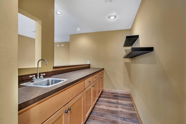 kitchen featuring dark countertops, dark wood-type flooring, baseboards, recessed lighting, and a sink