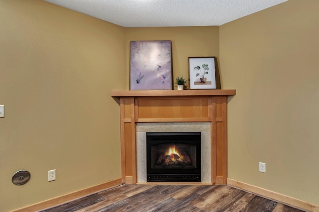 interior details with baseboards, a fireplace with flush hearth, a textured ceiling, and wood finished floors