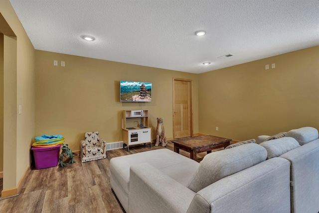 living room with wood finished floors, visible vents, baseboards, recessed lighting, and a textured ceiling