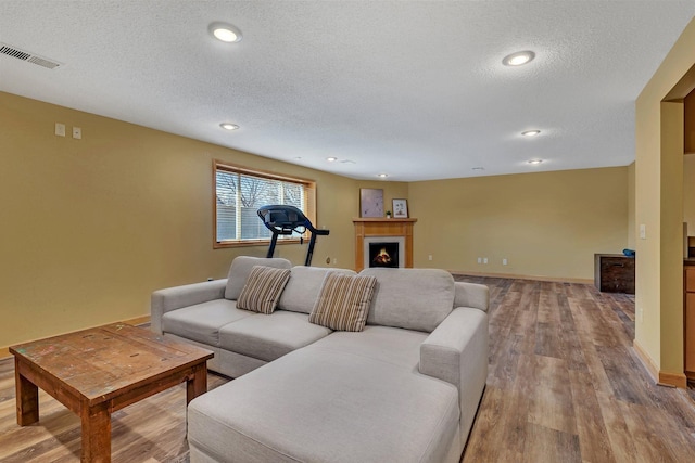 living room with visible vents, a warm lit fireplace, a textured ceiling, and wood finished floors