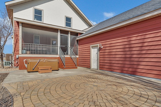 exterior space with a shingled roof, a patio, a sunroom, and a hot tub