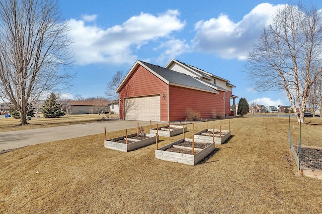 view of home's exterior featuring a vegetable garden, a yard, a garage, and driveway