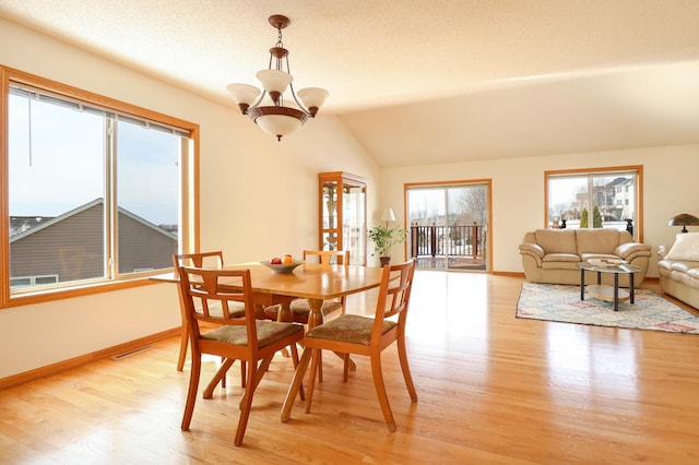 dining area featuring light wood-type flooring, lofted ceiling, a notable chandelier, and baseboards