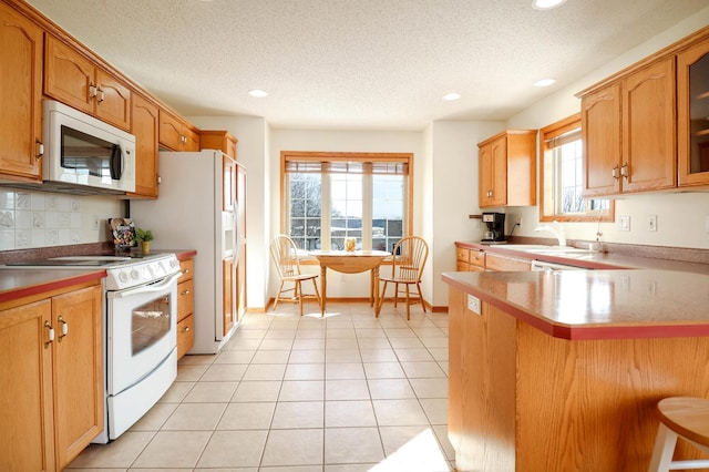 kitchen featuring a sink, white appliances, a healthy amount of sunlight, and a breakfast bar area