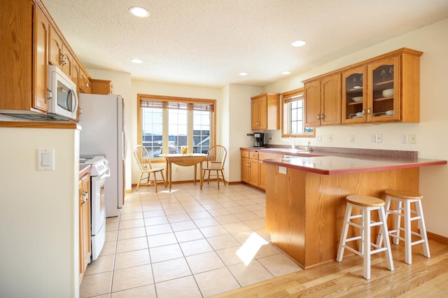 kitchen featuring a breakfast bar area, white microwave, a peninsula, electric stove, and glass insert cabinets