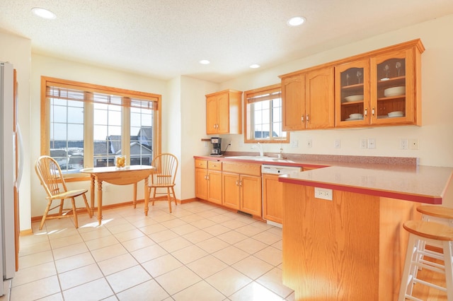 kitchen with a kitchen bar, a sink, paneled dishwasher, freestanding refrigerator, and a peninsula