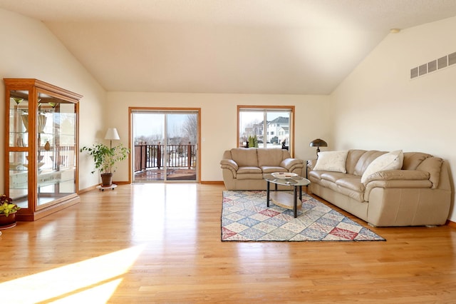 living area with light wood-type flooring, visible vents, baseboards, and high vaulted ceiling