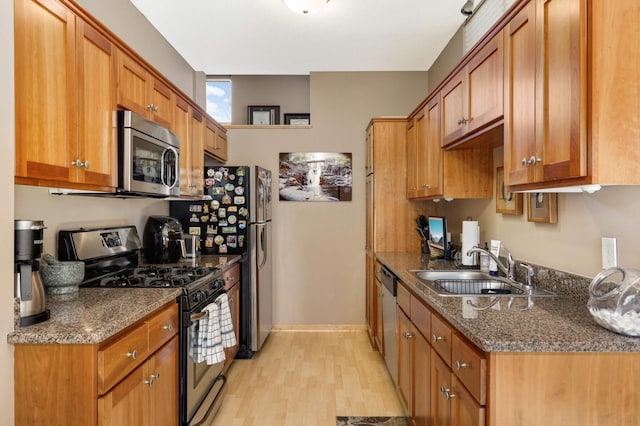 kitchen with dark stone counters, light wood-style flooring, appliances with stainless steel finishes, brown cabinetry, and a sink