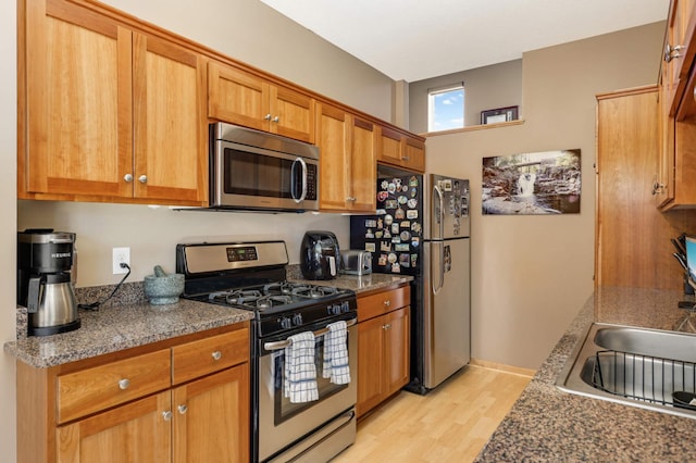 kitchen with a sink, brown cabinetry, light wood finished floors, and stainless steel appliances