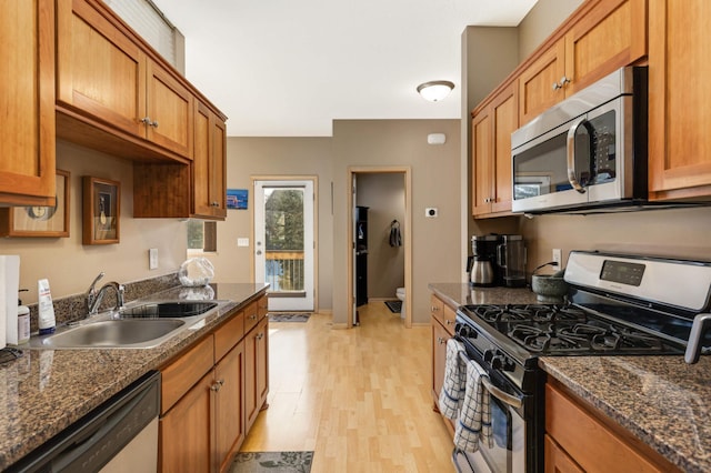 kitchen featuring dark stone counters, light wood-type flooring, brown cabinets, stainless steel appliances, and a sink