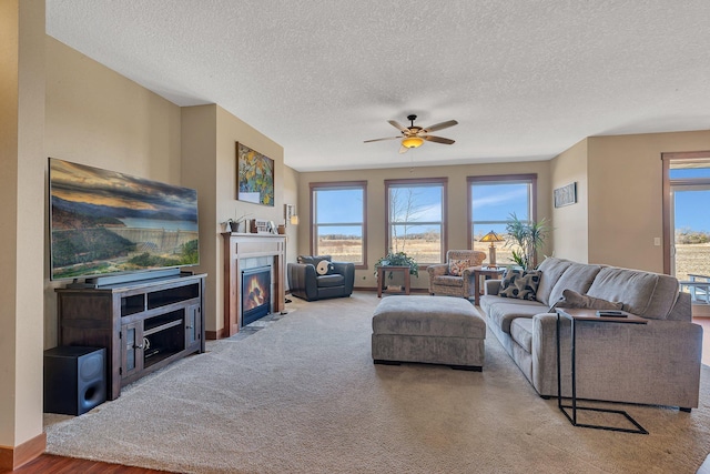 living room featuring a ceiling fan, a fireplace with flush hearth, carpet, and a textured ceiling