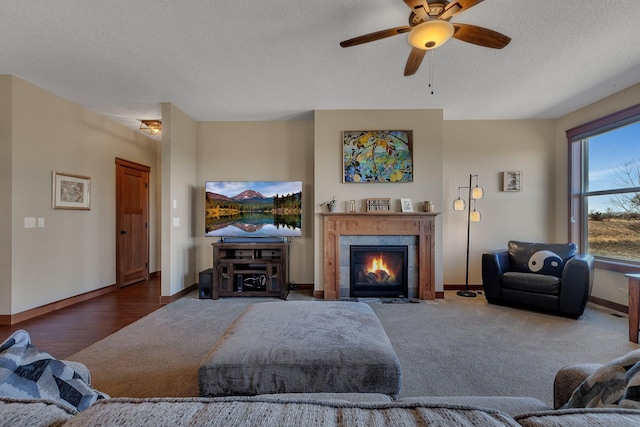 living room with a ceiling fan, a tiled fireplace, a textured ceiling, carpet, and baseboards