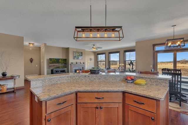 kitchen featuring light stone counters, dark wood-style floors, open floor plan, a center island, and a lit fireplace