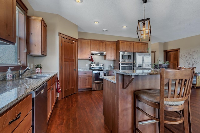 kitchen with under cabinet range hood, a breakfast bar, appliances with stainless steel finishes, dark wood-style floors, and a sink