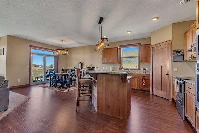 kitchen with brown cabinetry, stainless steel electric stove, a breakfast bar area, and dark wood-style flooring