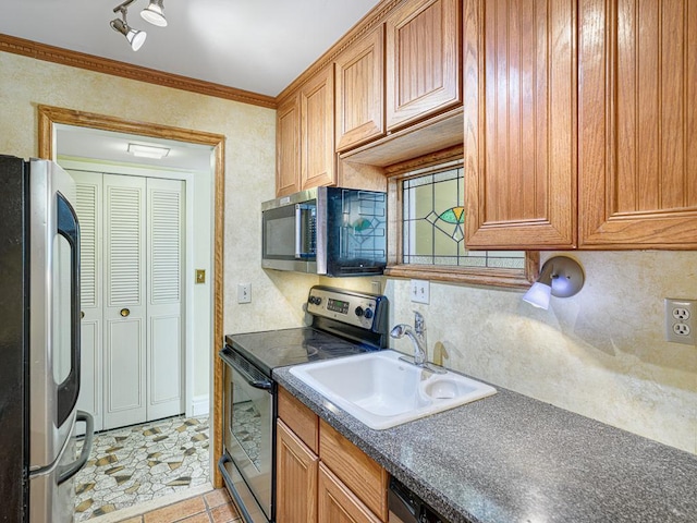 kitchen with brown cabinetry, a sink, ornamental molding, stainless steel appliances, and dark countertops