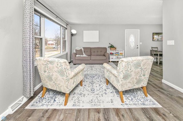 living room with visible vents, a textured ceiling, baseboards, and wood finished floors