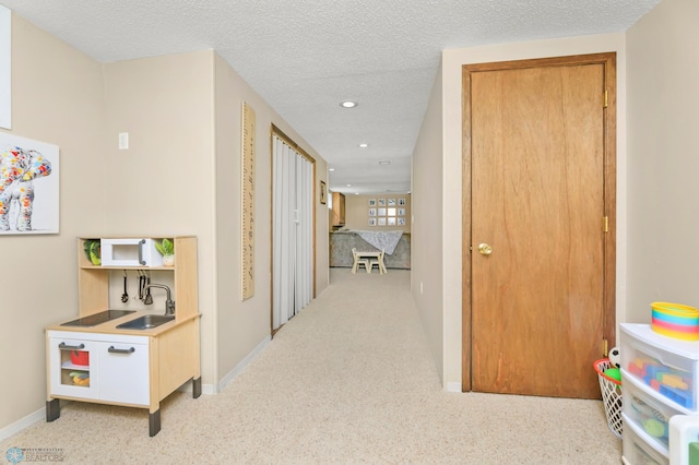 hall with baseboards, recessed lighting, a sink, a textured ceiling, and light colored carpet