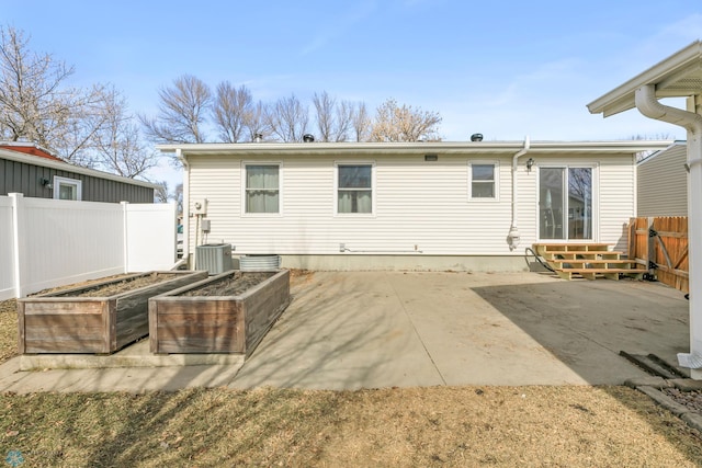 rear view of property with a vegetable garden, a patio area, fence, and central AC