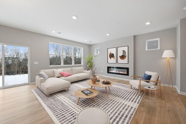 living room featuring light wood finished floors, a glass covered fireplace, recessed lighting, and baseboards