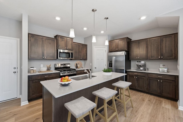 kitchen featuring a breakfast bar, a sink, dark brown cabinets, light wood-style floors, and appliances with stainless steel finishes