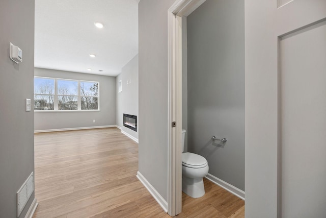 bathroom featuring visible vents, baseboards, toilet, wood finished floors, and a glass covered fireplace