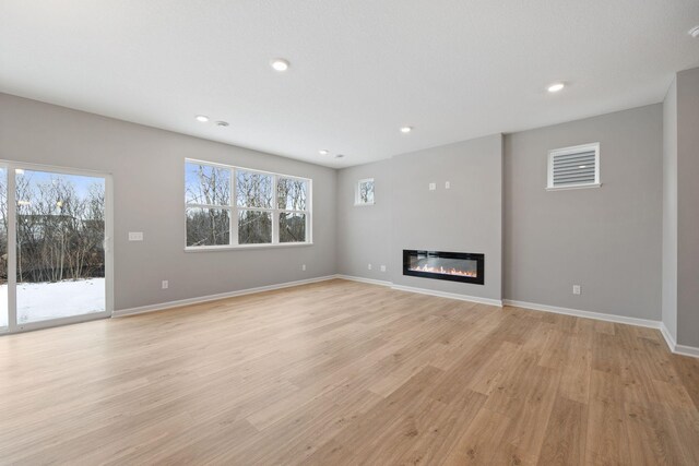 unfurnished living room featuring recessed lighting, light wood-type flooring, baseboards, and a glass covered fireplace