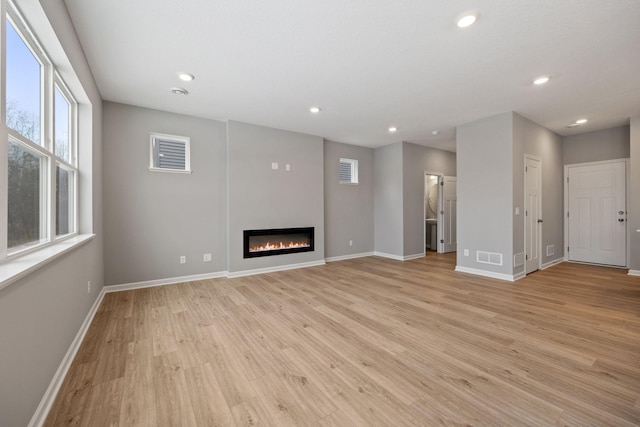 unfurnished living room featuring a glass covered fireplace, recessed lighting, light wood-style floors, and baseboards