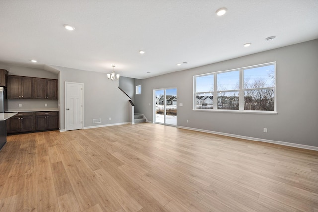 unfurnished living room with visible vents, baseboards, a chandelier, stairs, and light wood-style floors