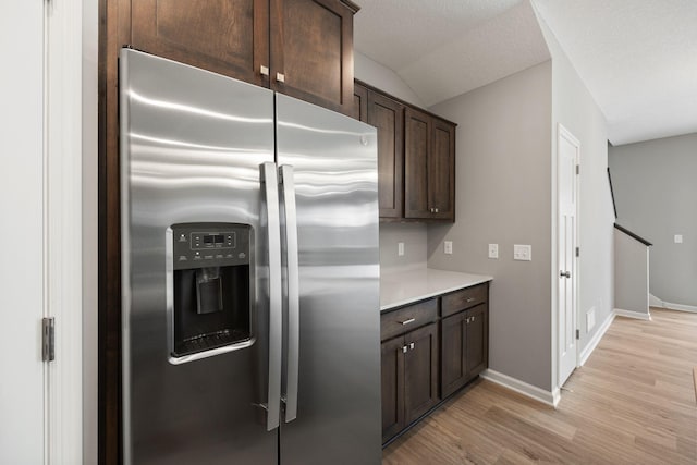 kitchen featuring baseboards, dark brown cabinetry, light countertops, light wood-style flooring, and stainless steel fridge