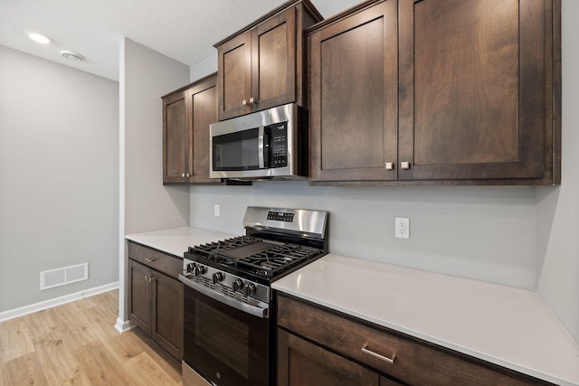 kitchen featuring visible vents, dark brown cabinets, light wood-type flooring, light countertops, and appliances with stainless steel finishes