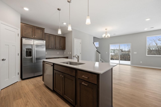 kitchen featuring an island with sink, a sink, stainless steel appliances, dark brown cabinets, and light wood-type flooring