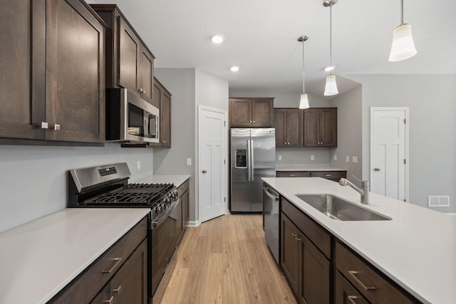 kitchen with dark brown cabinetry, stainless steel appliances, light countertops, and a sink