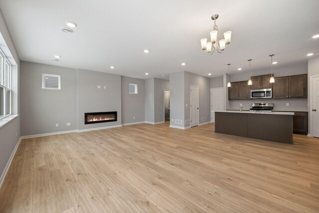 kitchen with dark brown cabinetry, open floor plan, light wood-style floors, a glass covered fireplace, and stainless steel appliances