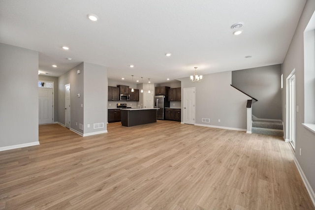 unfurnished living room with stairway, visible vents, baseboards, and light wood-style floors