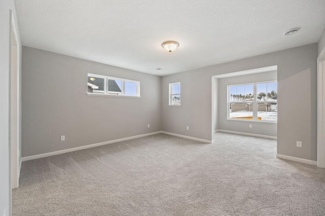 carpeted empty room featuring a healthy amount of sunlight, baseboards, and a textured ceiling