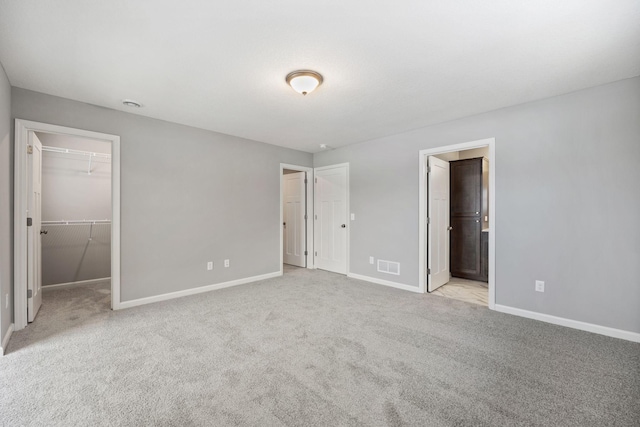 unfurnished bedroom featuring a walk in closet, baseboards, visible vents, and carpet floors