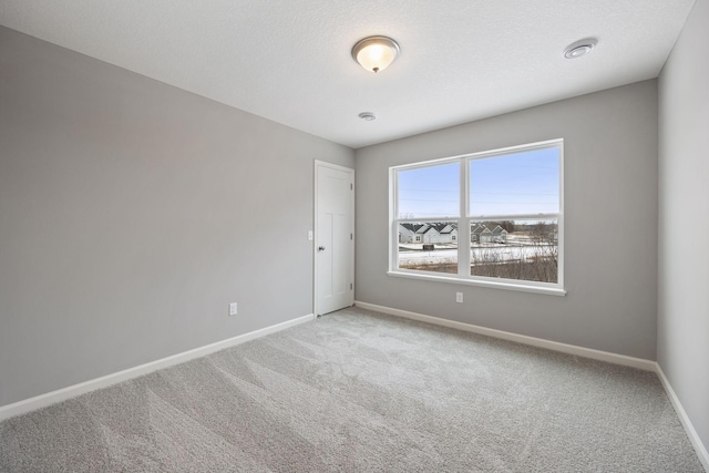 unfurnished room featuring light colored carpet, a textured ceiling, and baseboards