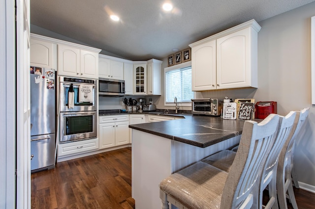 kitchen featuring dark wood-type flooring, a sink, dark countertops, stainless steel appliances, and a peninsula