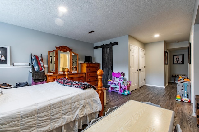 bedroom with visible vents, a textured ceiling, wood finished floors, a barn door, and baseboards