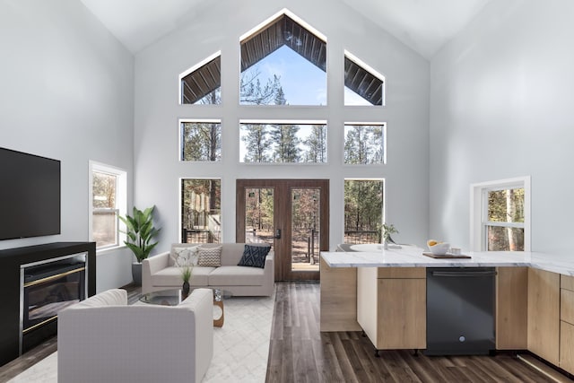 living room with plenty of natural light, dark wood-type flooring, french doors, and a glass covered fireplace