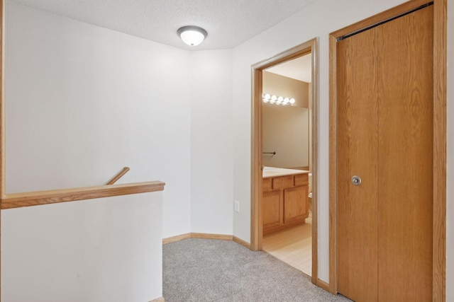 hallway featuring baseboards, light colored carpet, an upstairs landing, and a textured ceiling