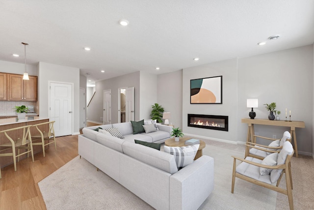 living room with light wood finished floors, baseboards, stairway, recessed lighting, and a glass covered fireplace